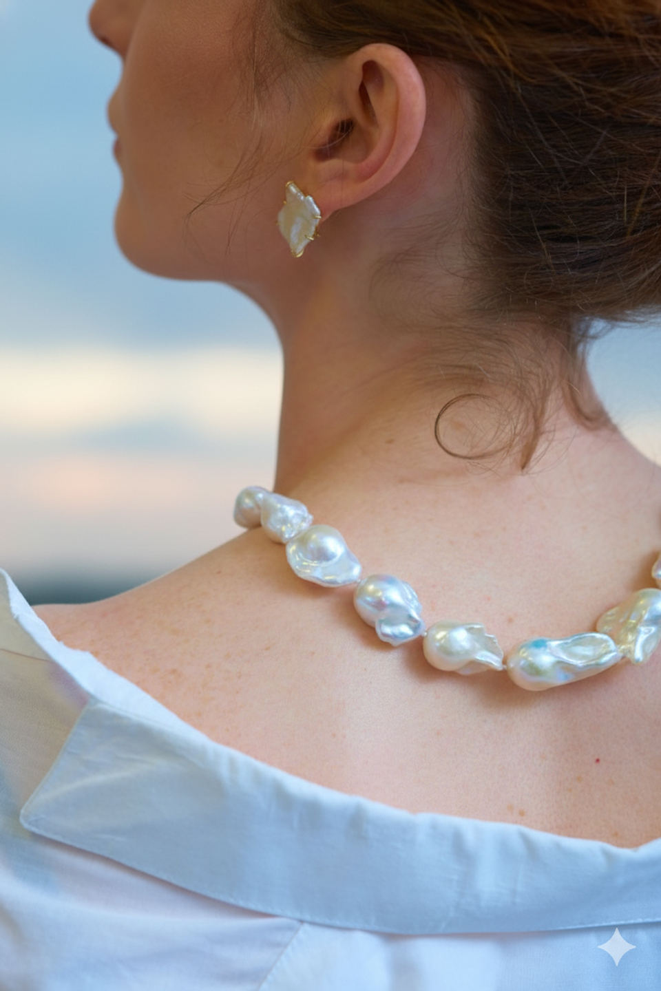 Collar y arete de perlas barrocas vistos desde la espalda, al atardecer.