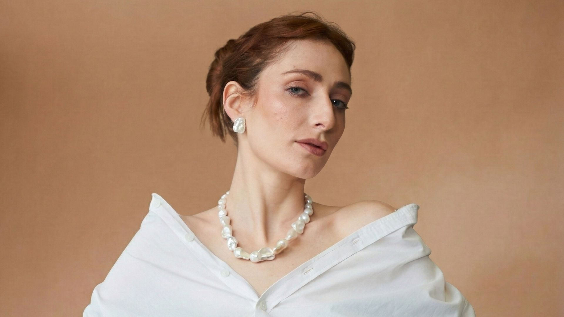 Modelo con collar y arete de perlas barrocas, sobre fondo terracota.